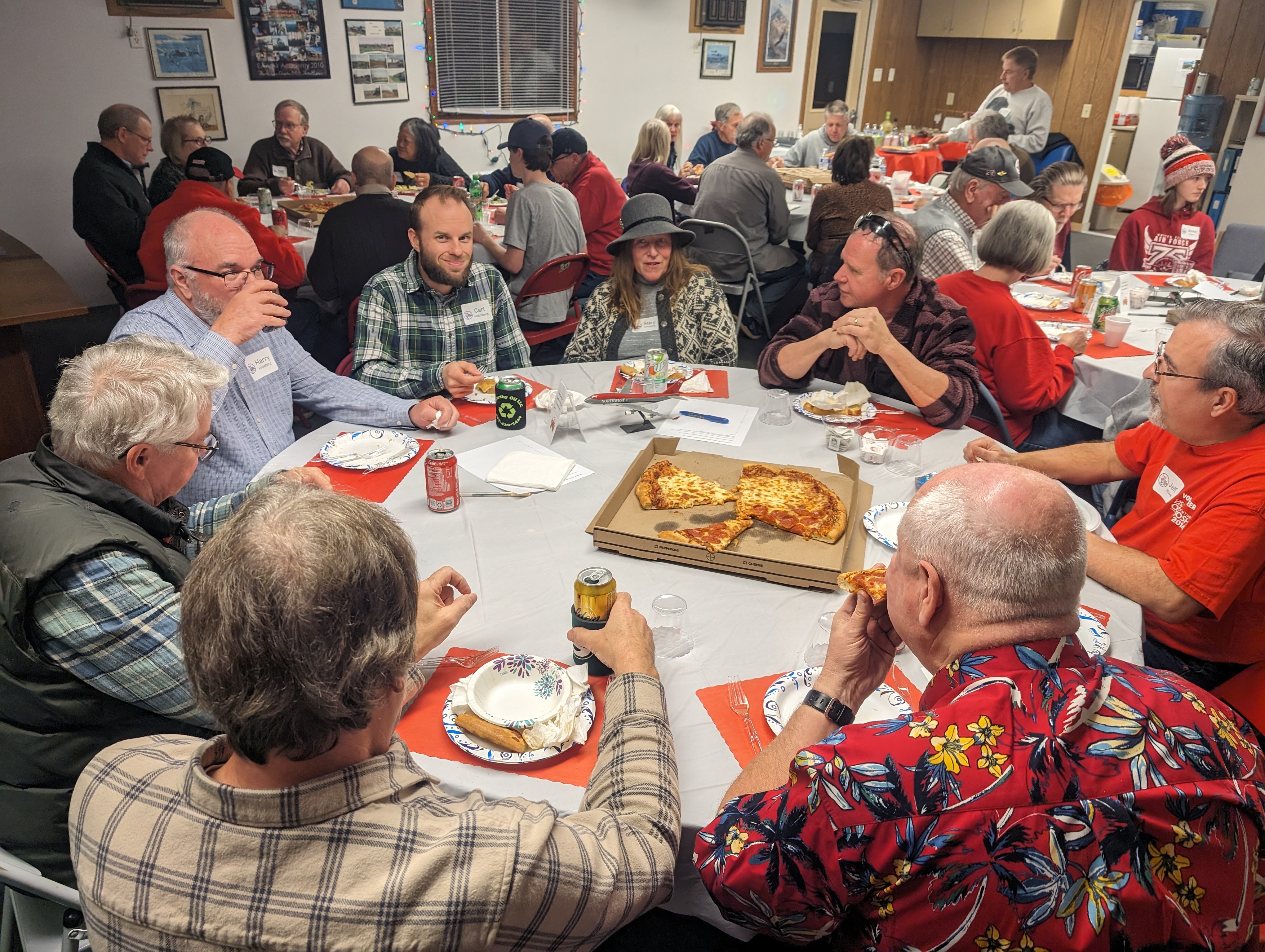 The 2023 Holiday Party. Shown are some of the tables with people sitting and eating pizza